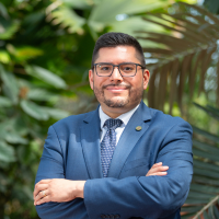 CPKD Superintendent in blue suit and tie with arms crossed, posing in front of greenery.